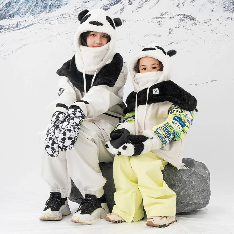 Two children in panda-themed outfits sitting on a rock in a snowy landscape.