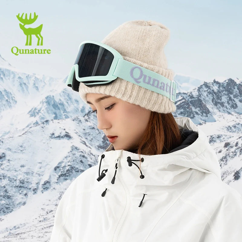 Person wearing a white jacket and beige beanie with Qunature goggles against a snowy mountain background